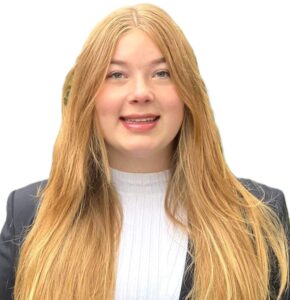 Eine junge Frau mit langen blonden Haaren trägt einen schwarzen Blazer und ein weißes Oberteil und lächelt vor einem schlichten weißen Hintergrund.