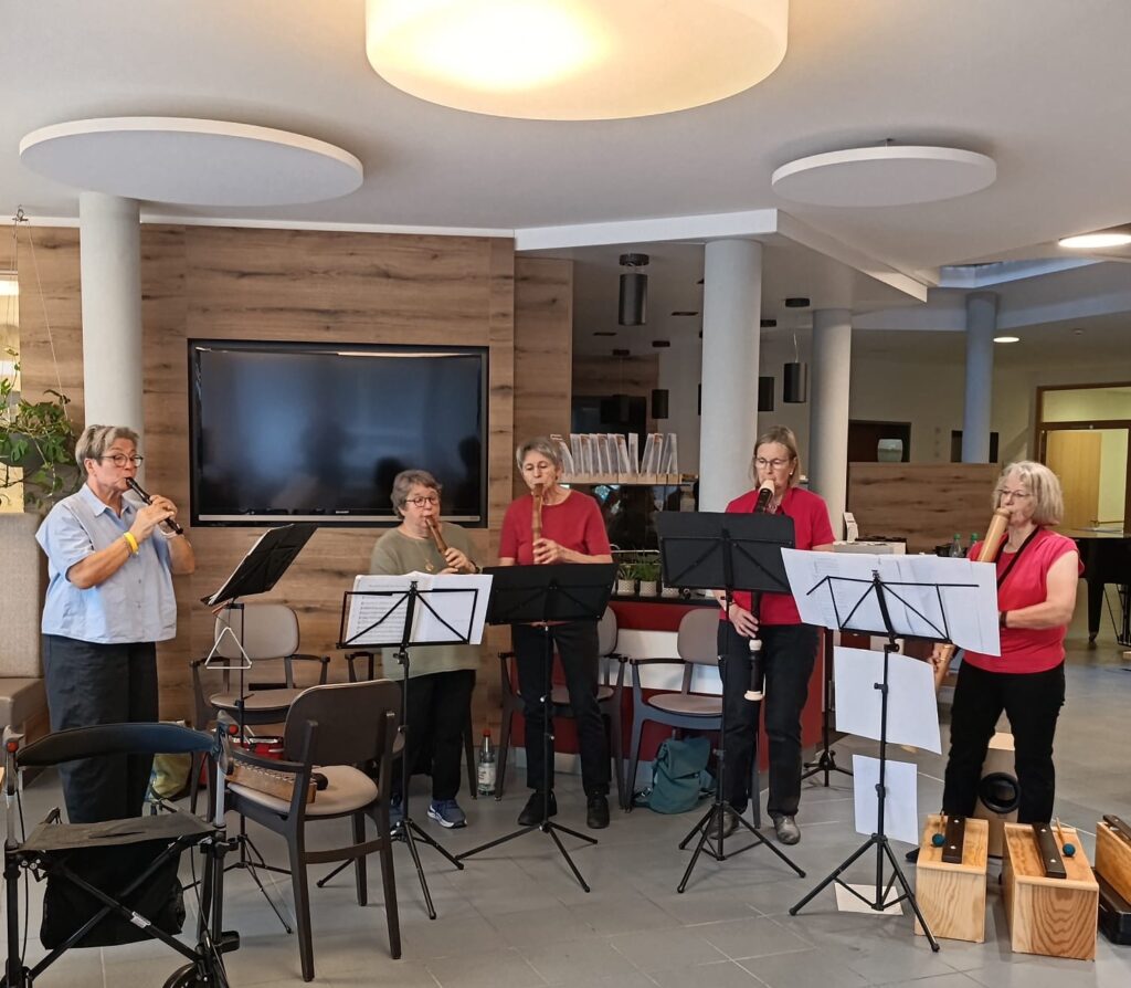 Fünf Musiker spielen auf Holzblockflöten, während sie in einem großen Raum hinter Notenständern stehen.